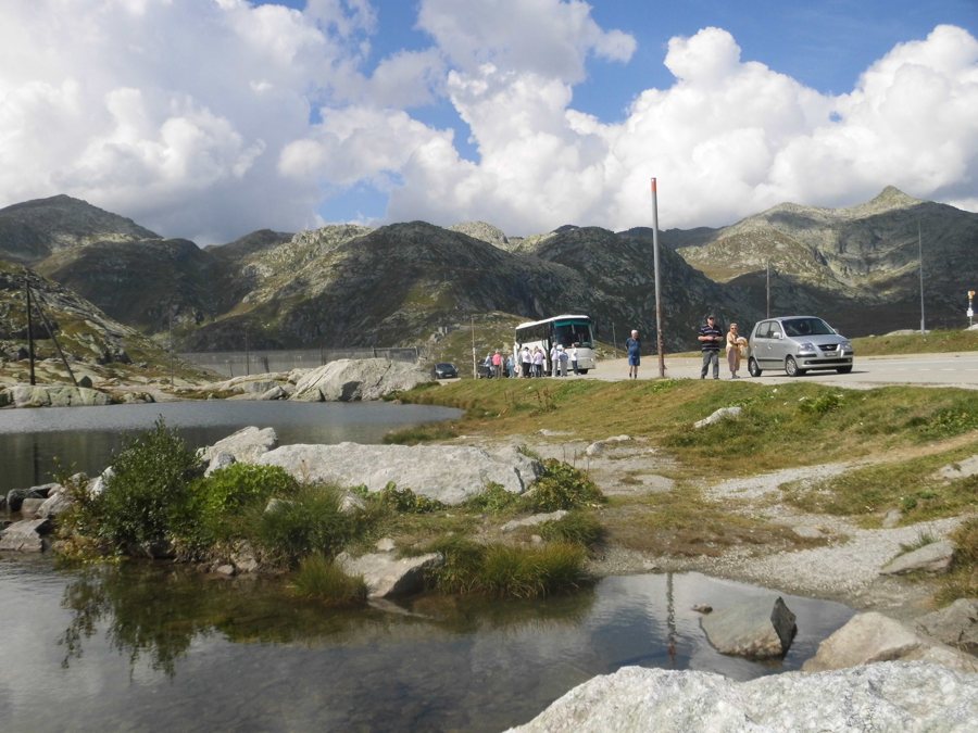 Bus und Reisende an einer Straße in einer alpinen Schweizer Berglandschaft